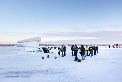 Hobbyflygplan står på snötäckt mark, personer har samlats runt det
