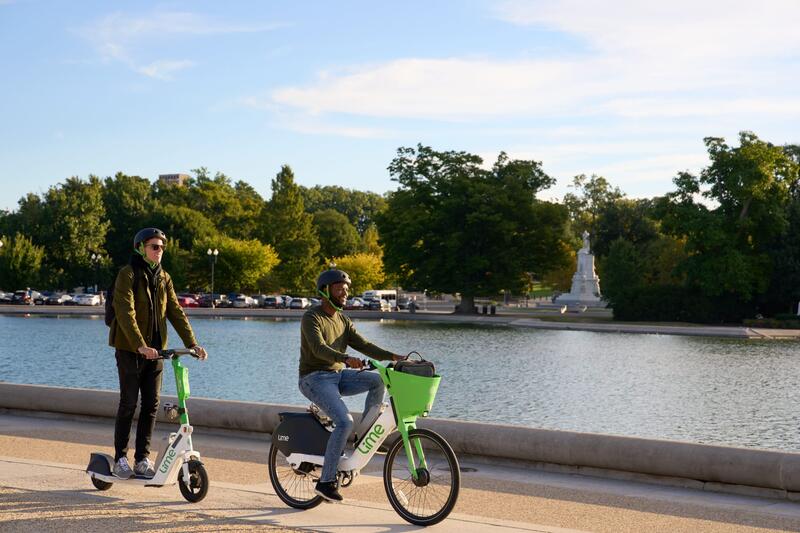 En person på elscooter och en på elcykel i en stadspark 