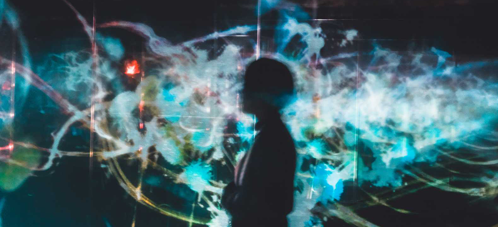 A person standing in front of some kind of a blurry, digital illustration. Photo: Unsplash.